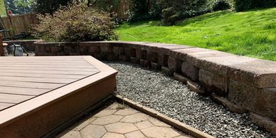 A backyard area with a retaining wall, gravel, and a wooden deck.