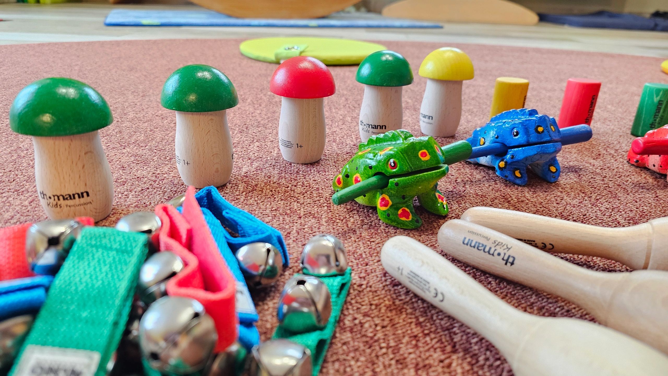 Bunte Holzspielzeuge und Perkussionsinstrumente auf Teppichboden.