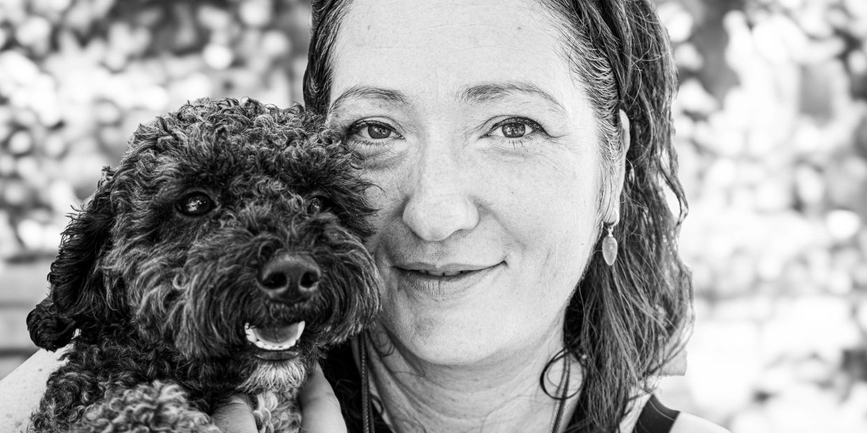 Eine lächelnde Frau hält einen lockigen Hund im Arm.