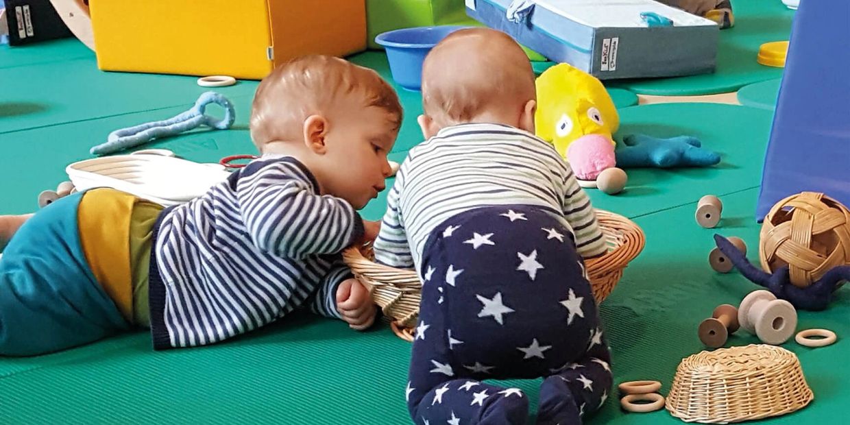 Zwei Babys spielen auf einer Spielmatte.
