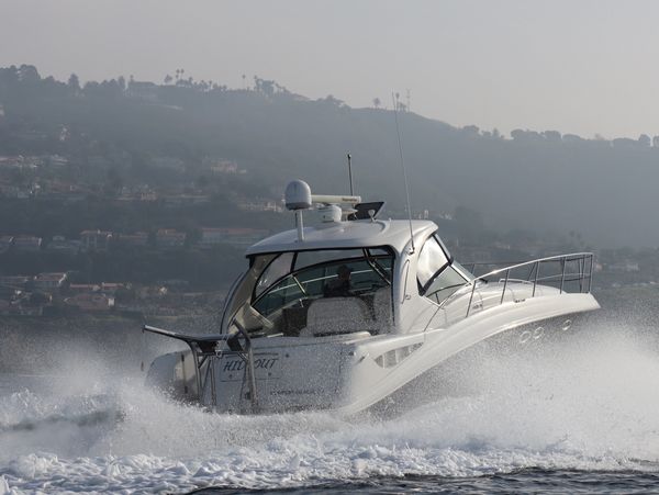 White motorboat speeding on water near a coastal town with hills.