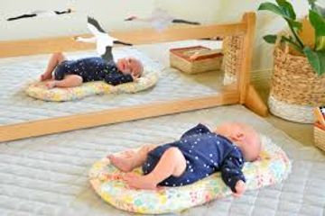 Baby lying on a pillow with a mirror reflecting the scene.