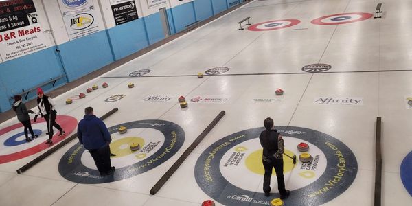 People playing curling indoors on an ice rink.