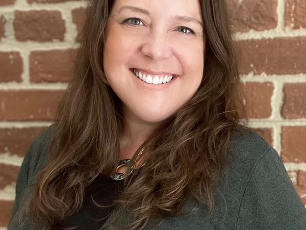 Smiling woman with long brown hair in front of a brick wall.