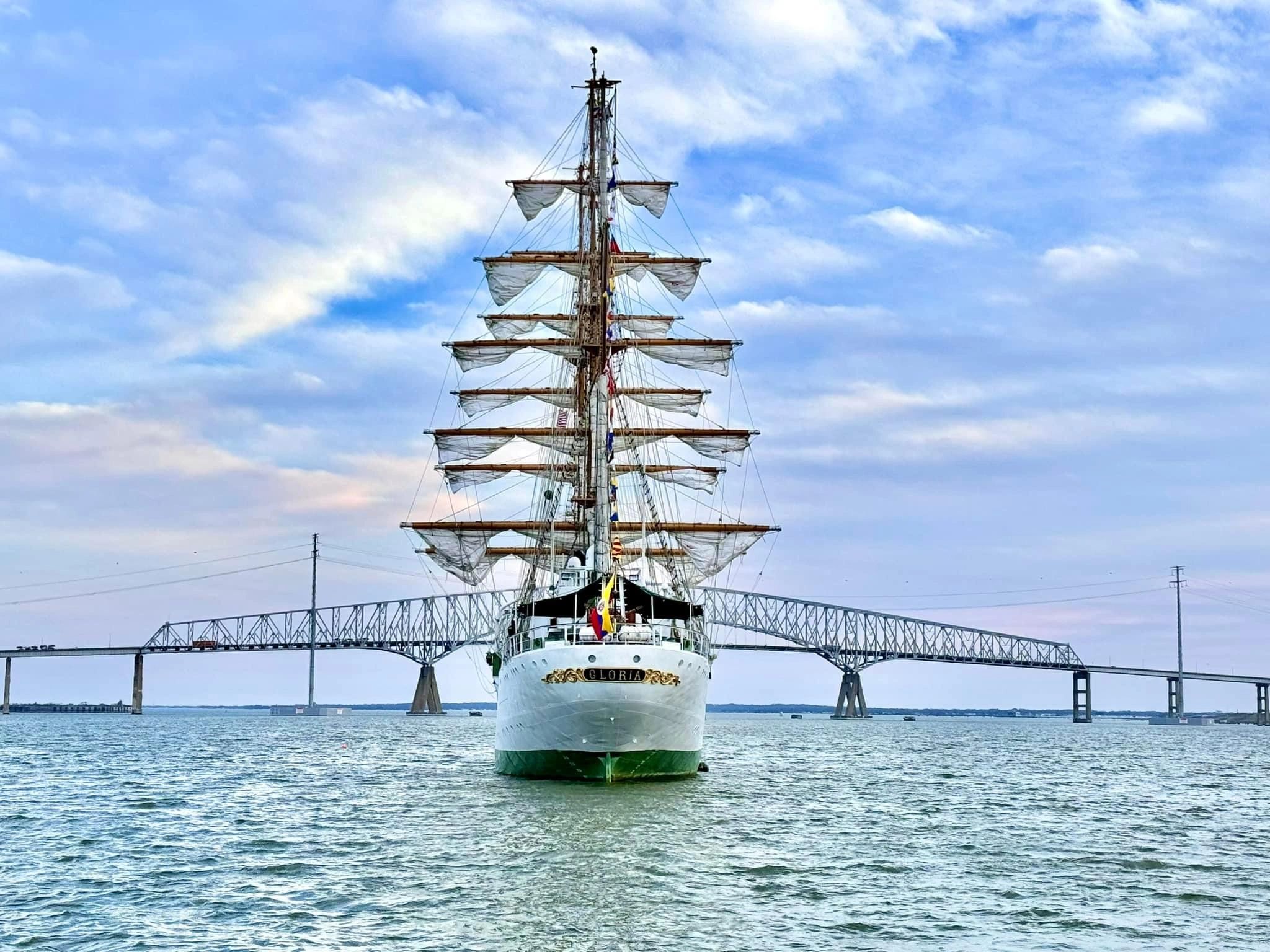 Tall ship named Gloria on the water with a bridge in the background.