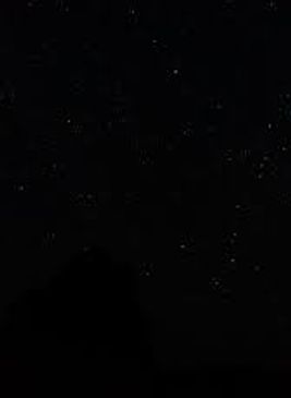 Night sky filled with stars above a dark silhouette of a mountain.