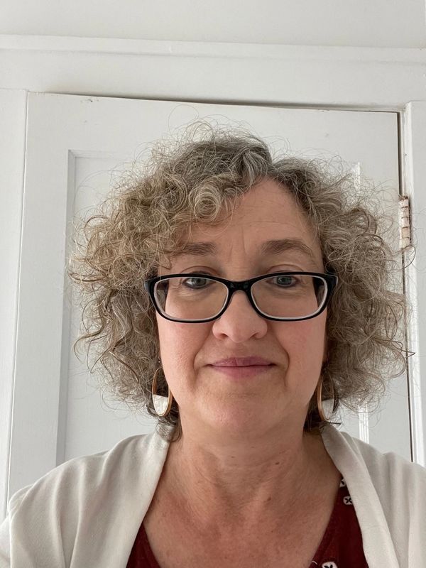 Middle-aged woman with curly hair and glasses smiling gently.