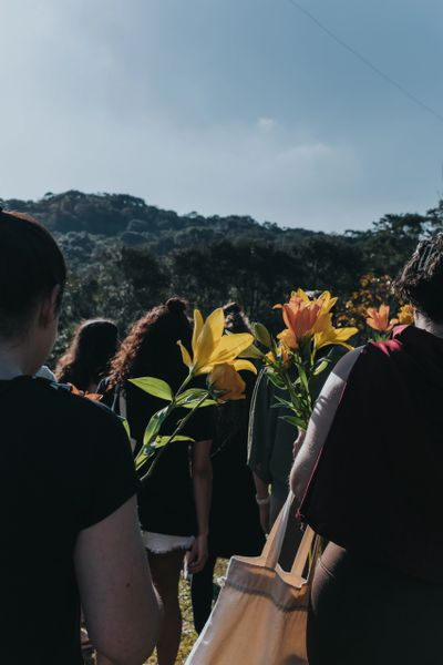People holding bright yellow lilies outdoors with a natural backdrop.
