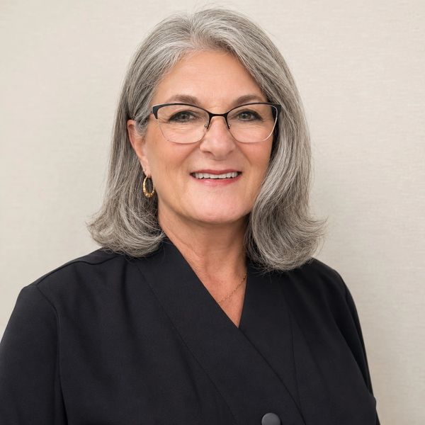 Smiling older woman with gray hair and glasses wearing a black outfit.