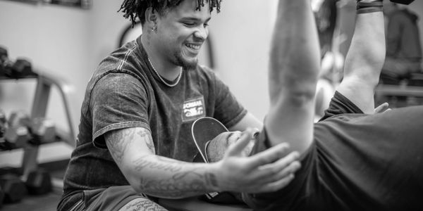 Trainer assists client with exercise in a gym setting, both smiling.
