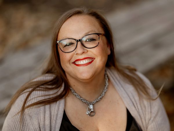 Smiling woman with glasses and red lipstick in a cozy sweater.