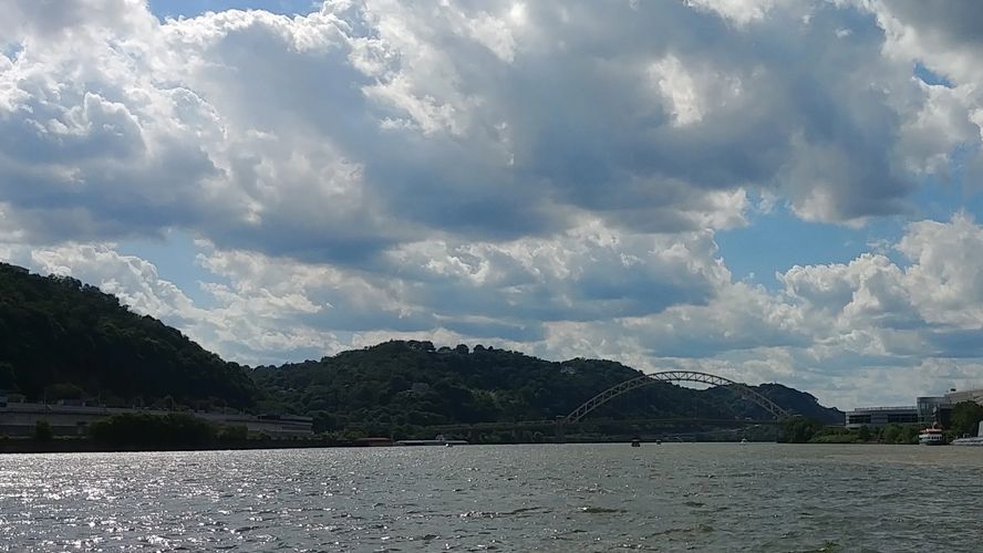 A scenic river view with hills, a bridge, and a partly cloudy sky.
