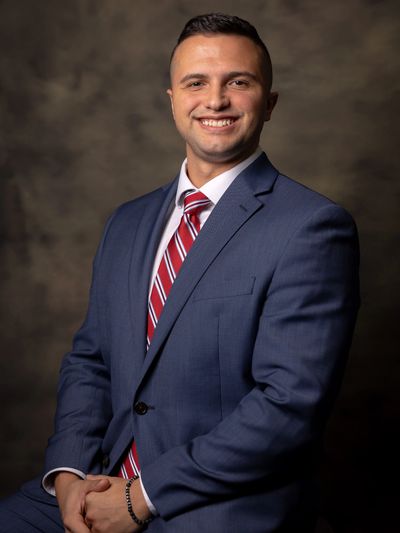 A confident man in a blue suit and red striped tie smiling.