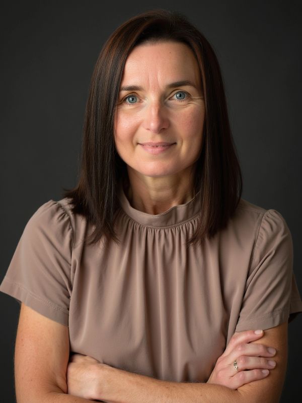 Smiling woman with crossed arms in a beige top.