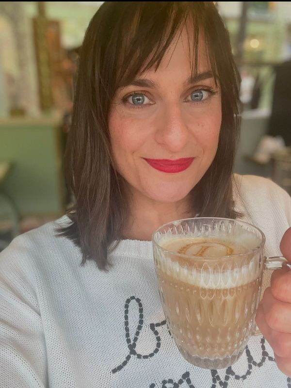 Woman holding a glass cup of coffee, smiling.