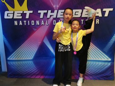 Two girls posing at a dance competition with medals and trophy.