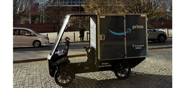 Delivery workers in high-visibility vests standing beside Amazon Prime vans at loading bays.