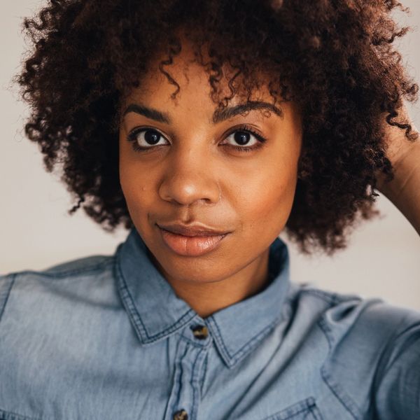 Close-up of a woman with curly hair wearing a denim shirt.
