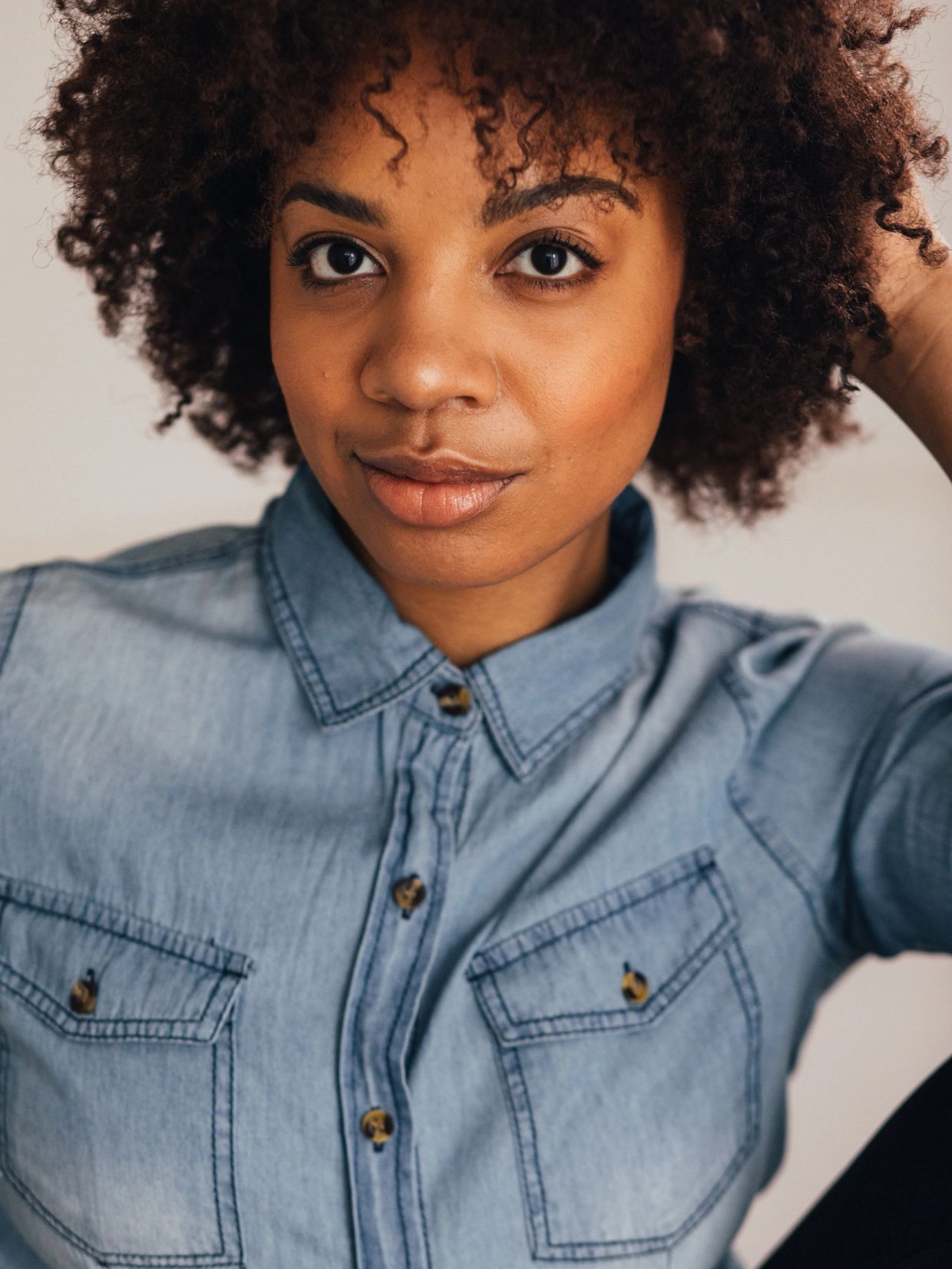 Close-up of a woman with curly hair wearing a denim shirt.