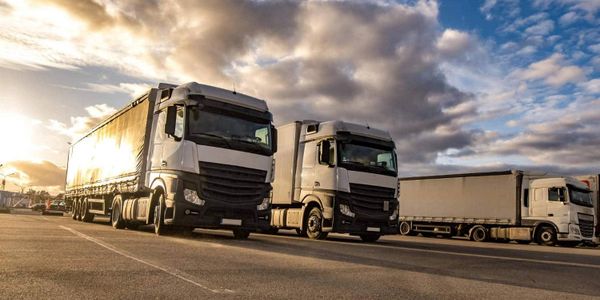 Three white cargo trucks parked under a dramatic sky at sunset.