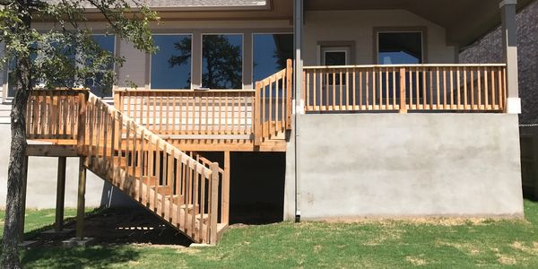 Wooden deck and stairs attached to a house with a grassy yard.