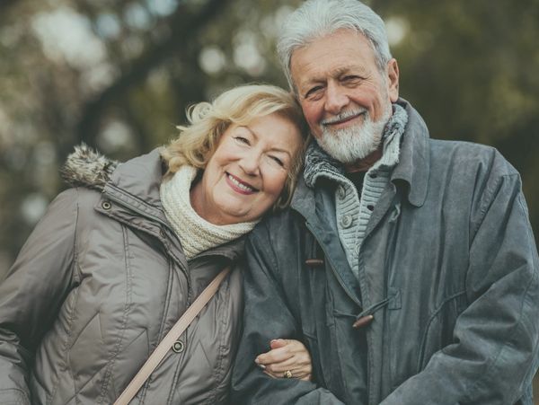 Happy elderly couple smiling outdoors in winter clothing.