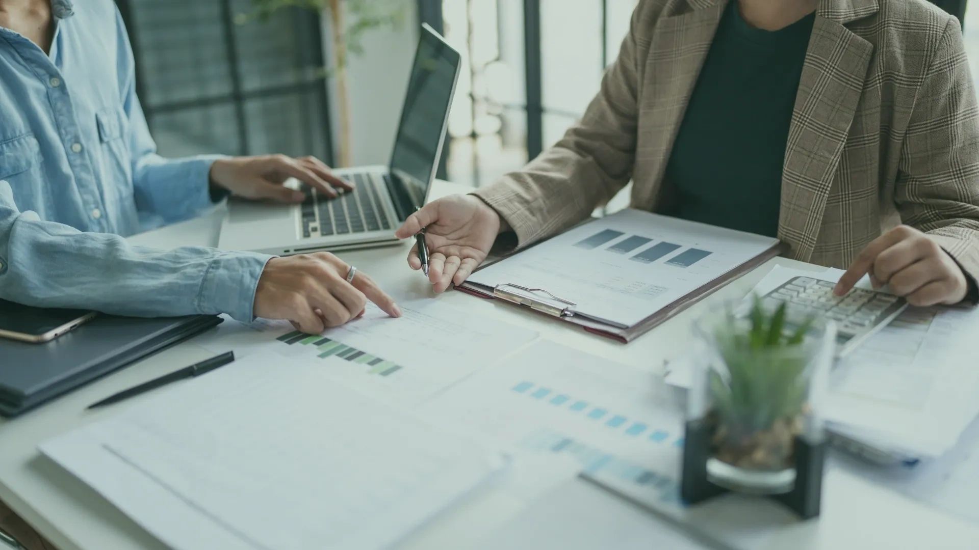 Two professionals working on financial documents and charts at a desk.