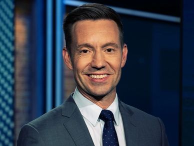 Man in a suit smiling confidently in a studio setting.