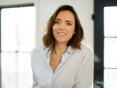 Smiling woman in a light blue shirt leaning on a white surface.