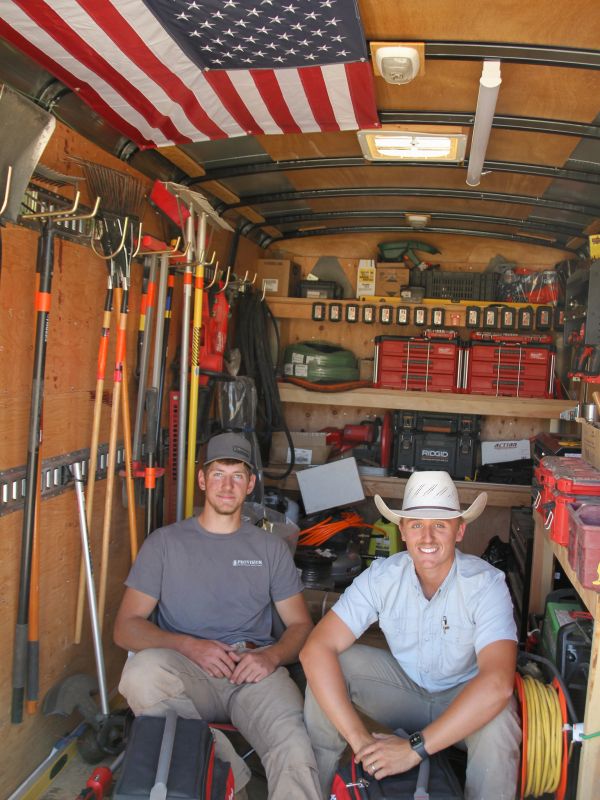 Two men sitting inside a well-organized tool storage truck with an American flag.