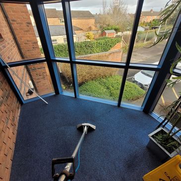 Empty blue-carpeted room with large windows and a mop.
