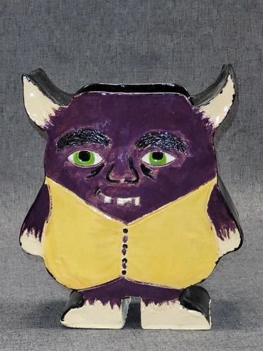Purple and yellow ceramic monster figurine with green eyes and horns.