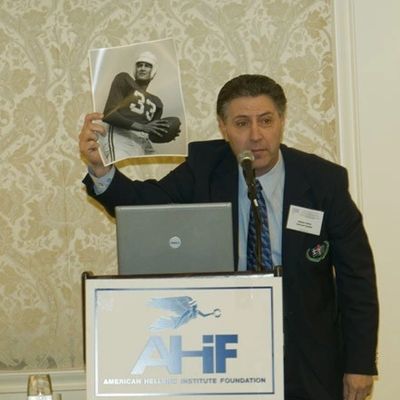 Man presenting a black-and-white baseball photo at an American Hellenic Institute event.