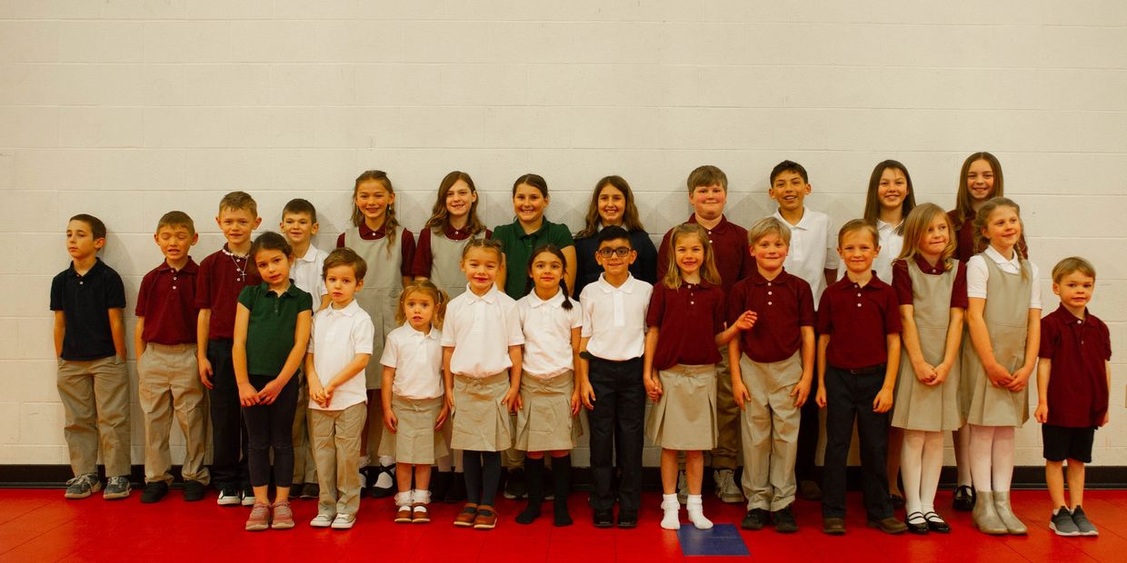 A group of school children in uniforms standing in rows against a wall.