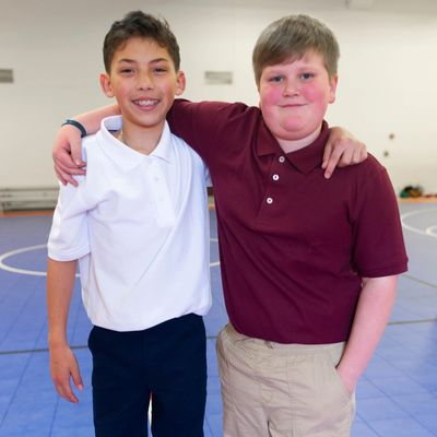 Two boys smiling with arms around each other in a gymnasium.