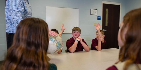 Students raising hands in a classroom discussion.