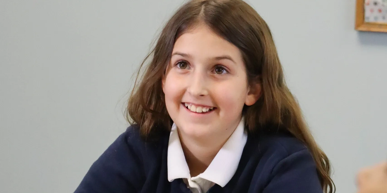 Smiling schoolgirl in uniform with long brown hair.