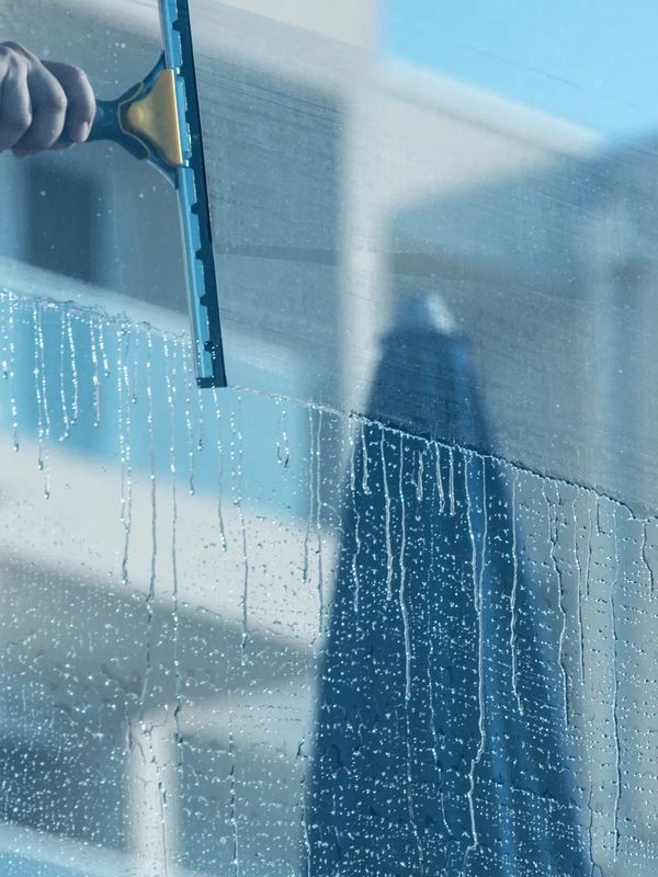 A person cleaning a window with a squeegee, revealing a clear view.