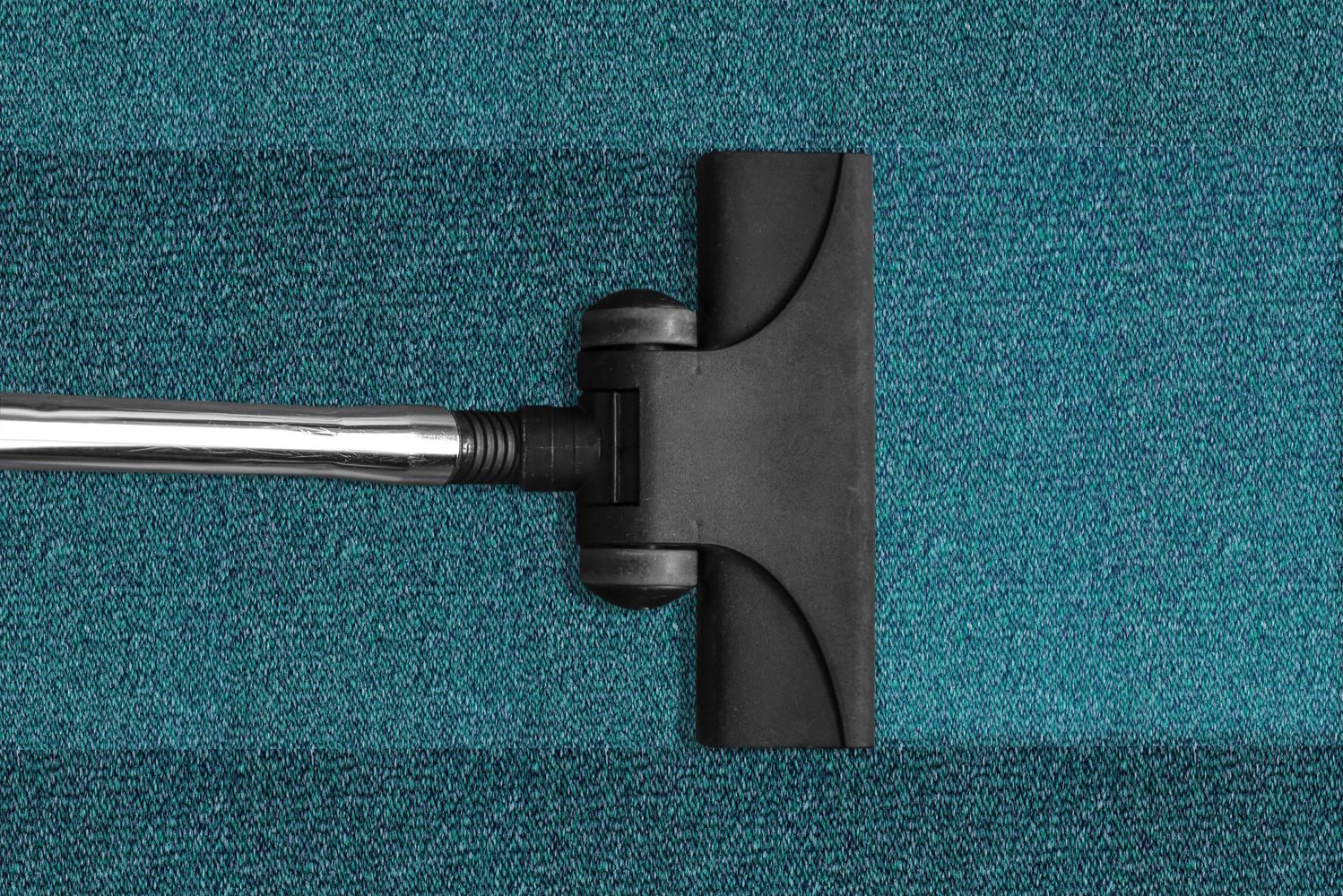 Vacuum cleaner cleaning a teal carpet, showing a visible clean path.