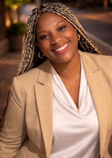 Smiling woman with braided hair wearing a beige blazer and white blouse.