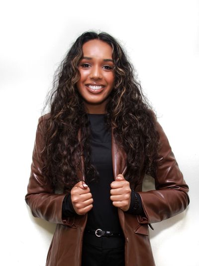 Smiling woman with long curly hair in a brown leather jacket.