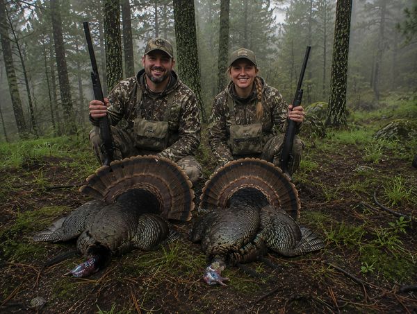 Dos cazadores posan con sus pavos capturados en un bosque.
