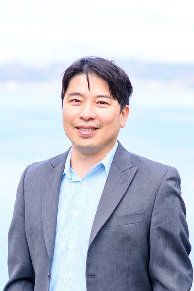 Smiling man in gray suit with light blue shirt outdoors.
