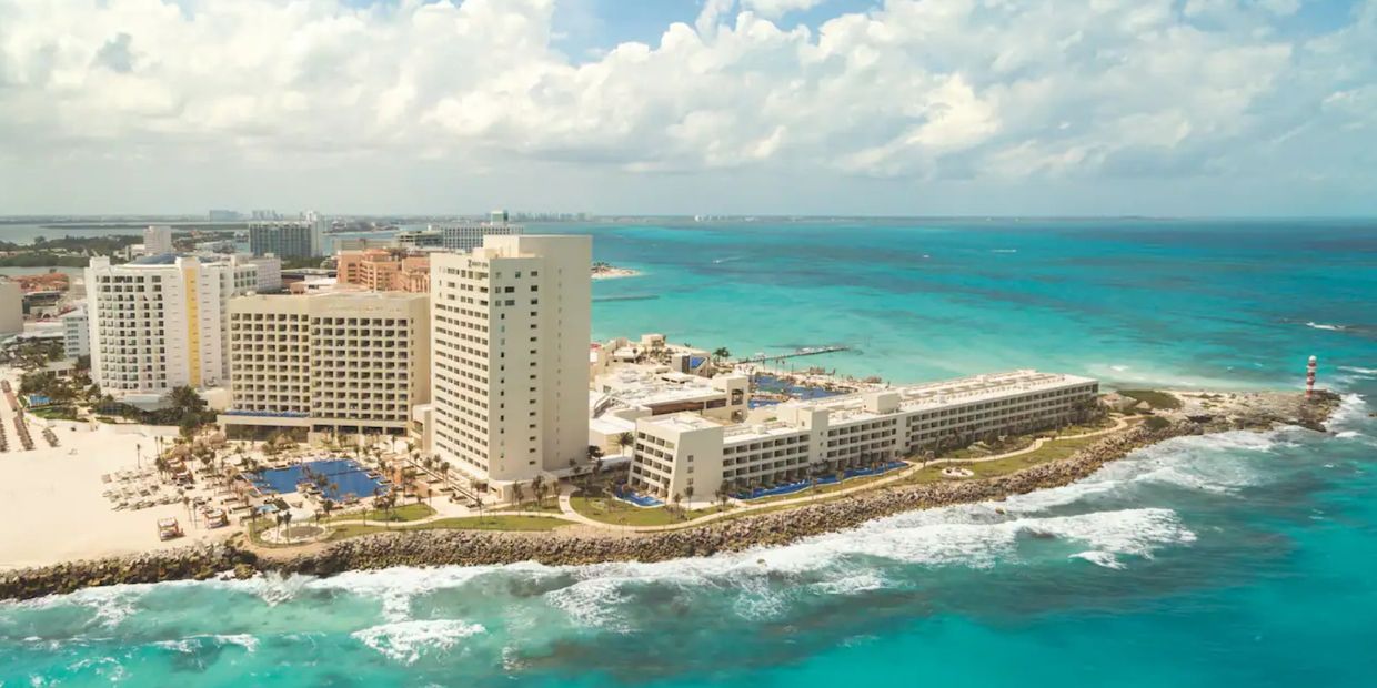 Oceanfront resort with pools and sandy beach under partly cloudy skies.