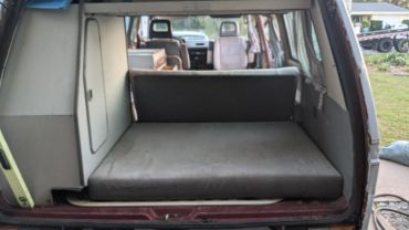 Interior of a van with a foldable bed and seating area.