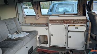 Interior of an old camper van with worn-out cabinets and a gray couch.