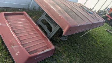 Two rusty red truck beds placed on grass beside a white fence.