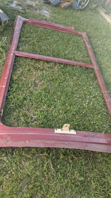 A rusty red metal frame lying on grass with a latch mechanism.