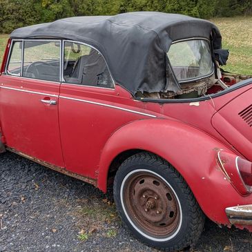 Old red convertible car with torn soft top.