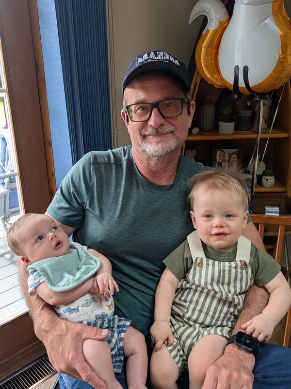 Grandfather holding two young grandchildren, smiling warmly indoors.